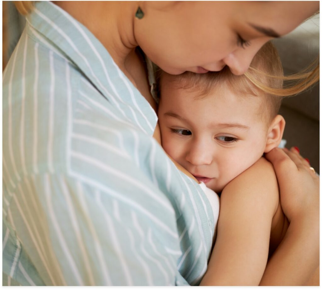 cropped-image-of-tender-caring-young-mother-craddling-her-sleepy-baby-in-arms-singing-song-to-him-kissing-on-forehead-mom-hugging-one-ye